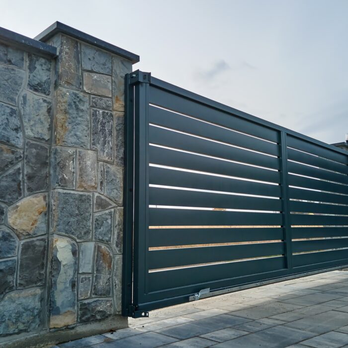 Wide automatic sliding gate with remote control installed in high stone fense wall