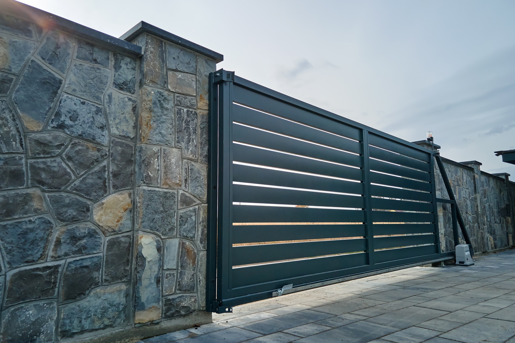 Wide automatic sliding gate with remote control installed in high stone fense wall